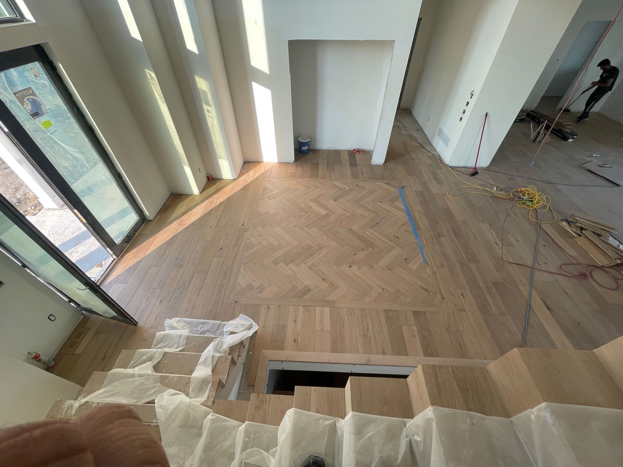 Open hardwood flooring installation with a herringbone inlay and stair detail