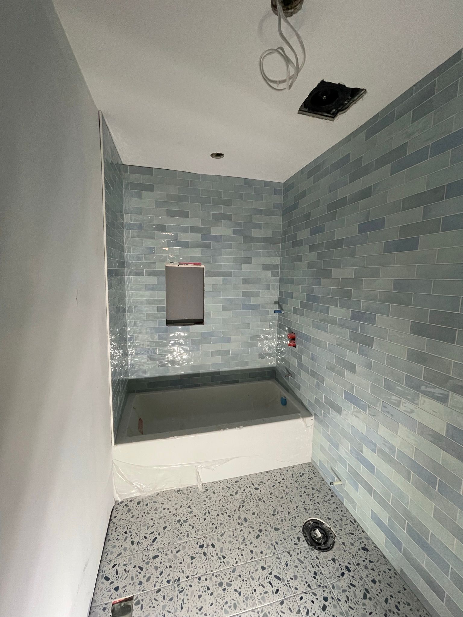 Washroom renovation with blue subway shower tile and terrazzo-look floor tile